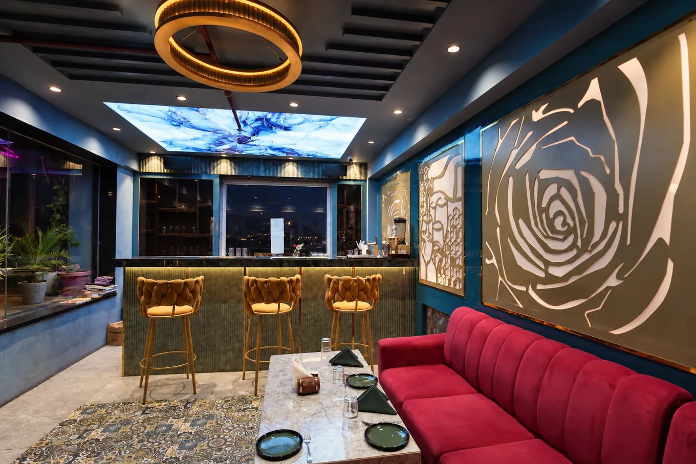 Blue lounge with a red sofa, marble table and gold bar stools