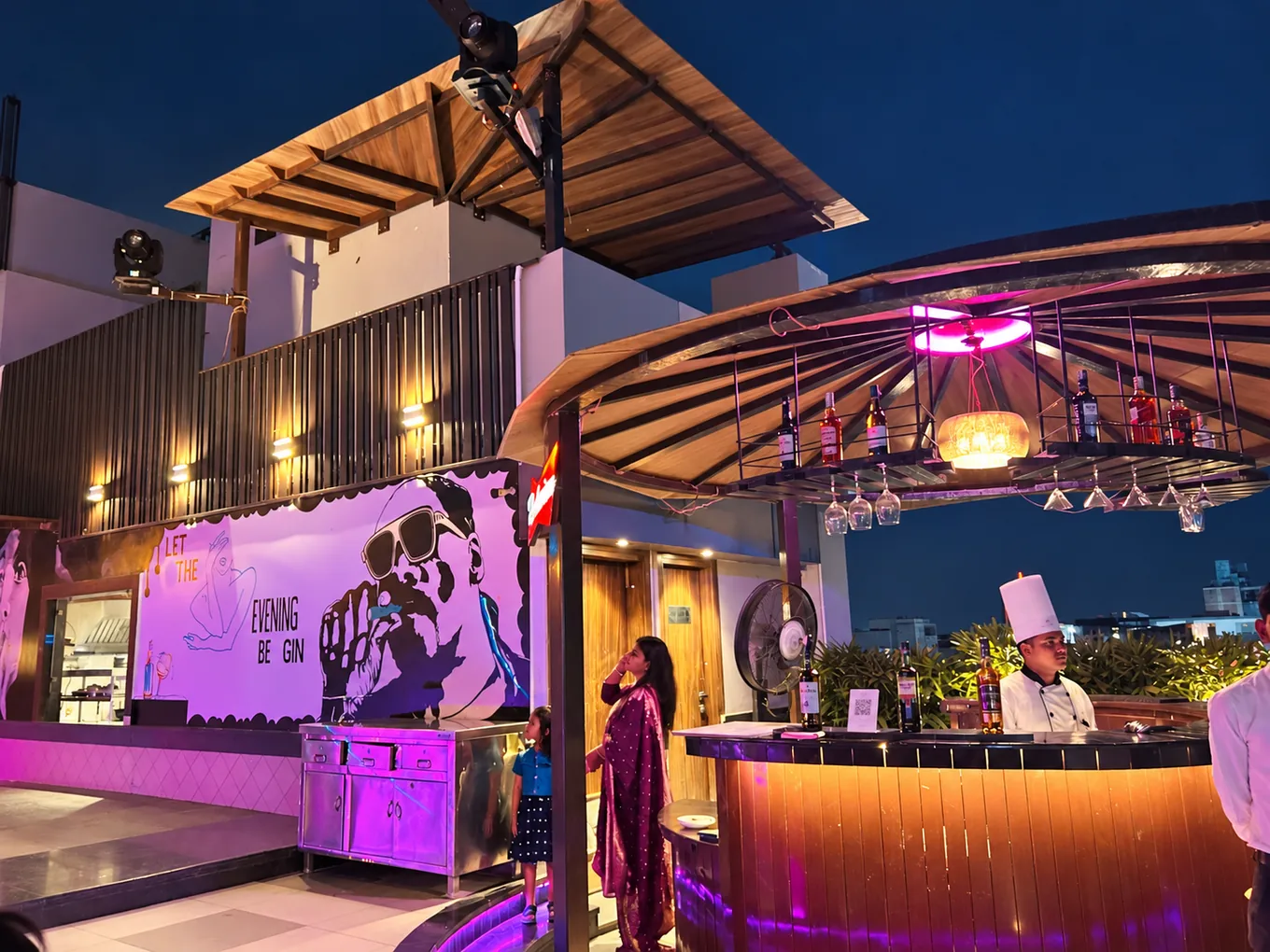 Staff beside the circular rooftop bar under purple evening lighting