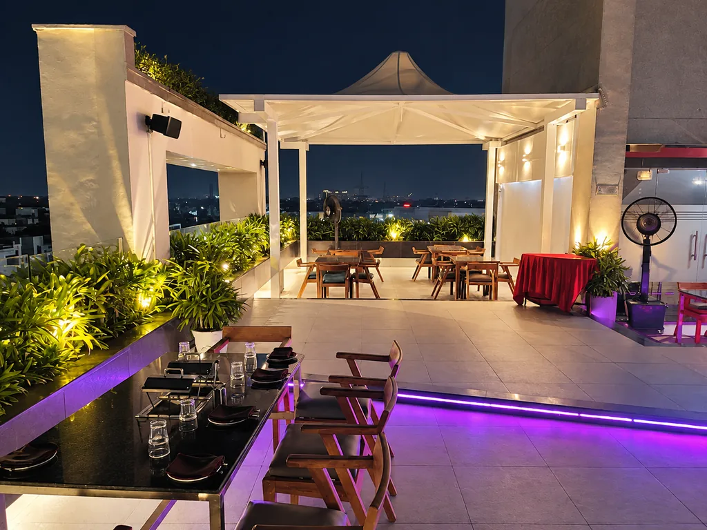 Wide nighttime terrace view with dining tables and a lit white canopy