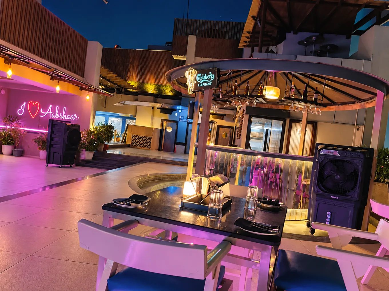 Circular rooftop bar and dining table under magenta evening lights