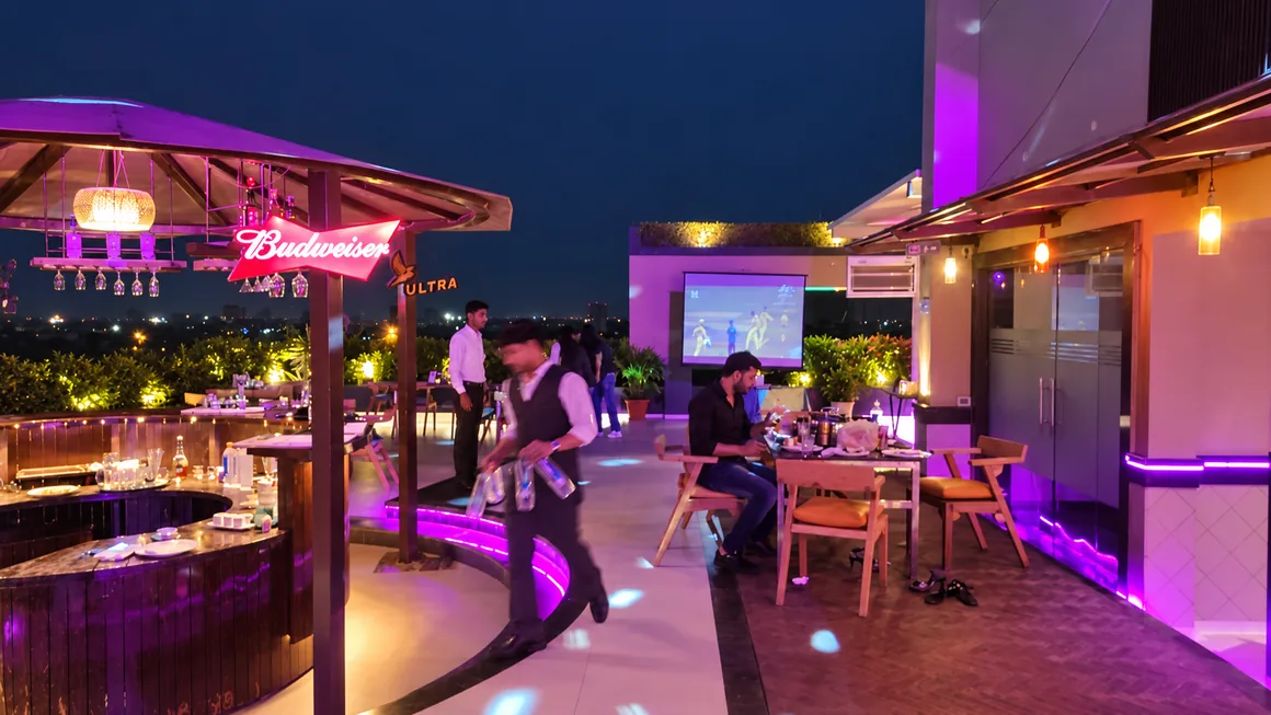 Guests and serving staff near the rooftop bar in purple evening light