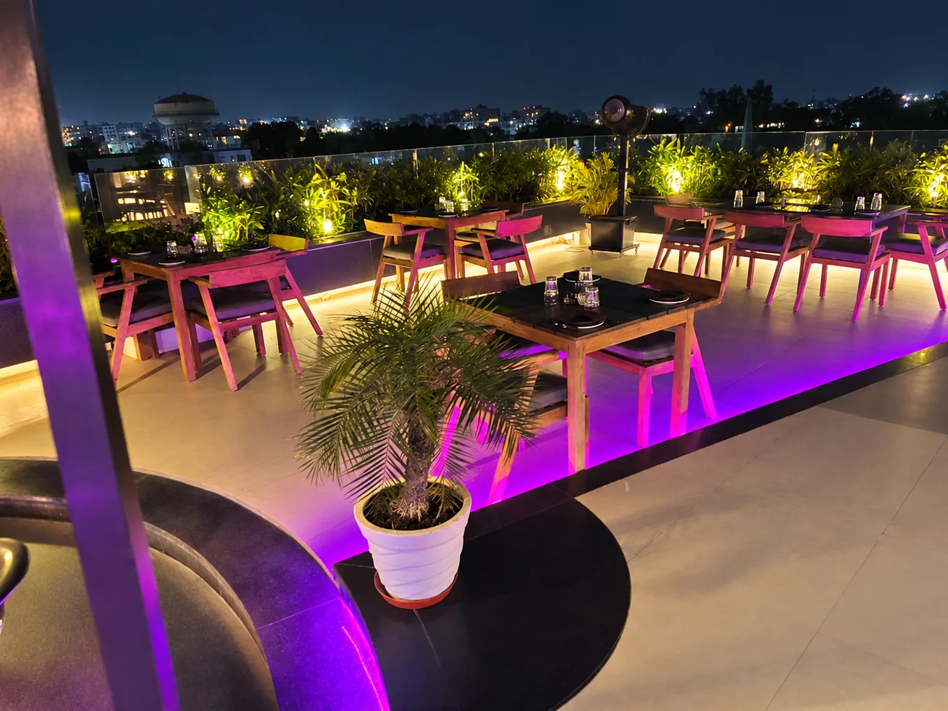 Outdoor dining tables beside illuminated plants and purple accent lights